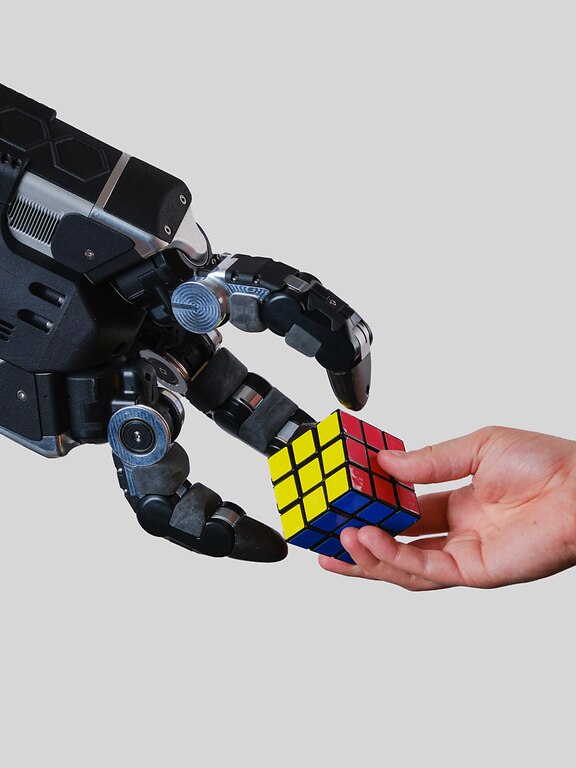A human hands a rubik's cube to a robot hand, symbolizing innovation and advanced robotics.