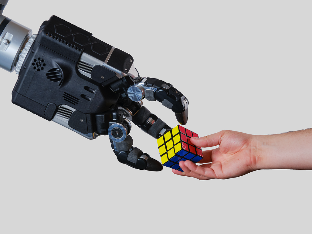A human hands a rubik's cube to a robot hand, symbolizing innovation and advanced robotics.