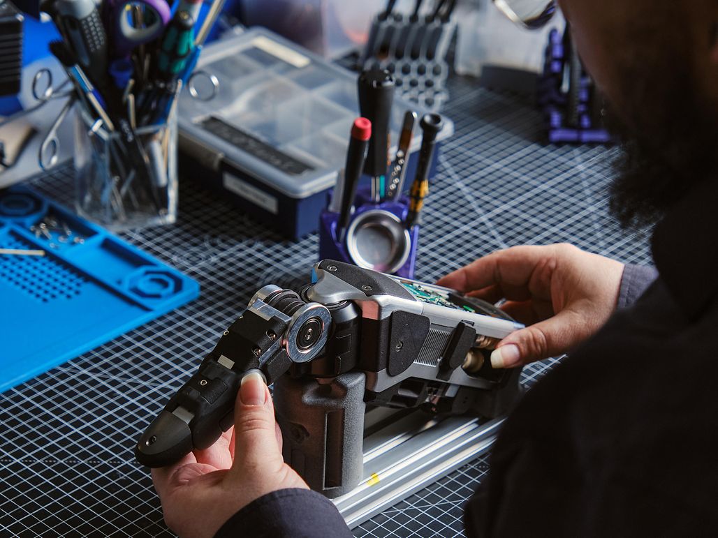 A man in a black shirt assembles a robotic hand.