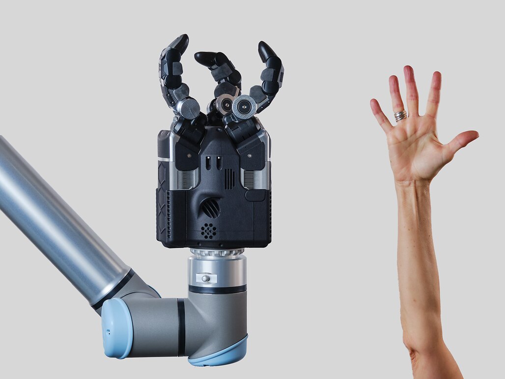 A human hand is reaching up to a robotic arm, representing the different sizes.